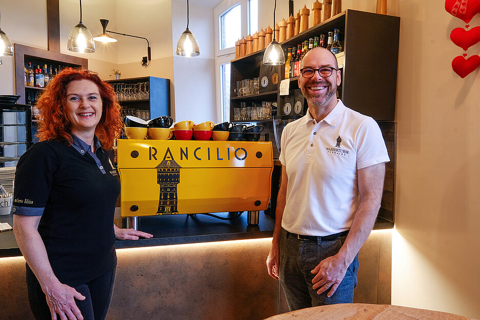 Mirabelle und Alain Caboussat freuen sich über die Rancilio Specialty RS1 Kaffeemaschine in der Sonderfarbe Gelb inklusive Wasserturm-Aufdruck.
