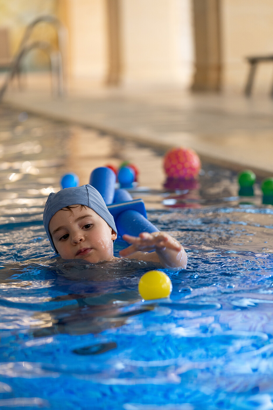 Child swimming with floatation device and playing with ball in indoor pool Child swimming with floatation device and playing with ball in indoor pool